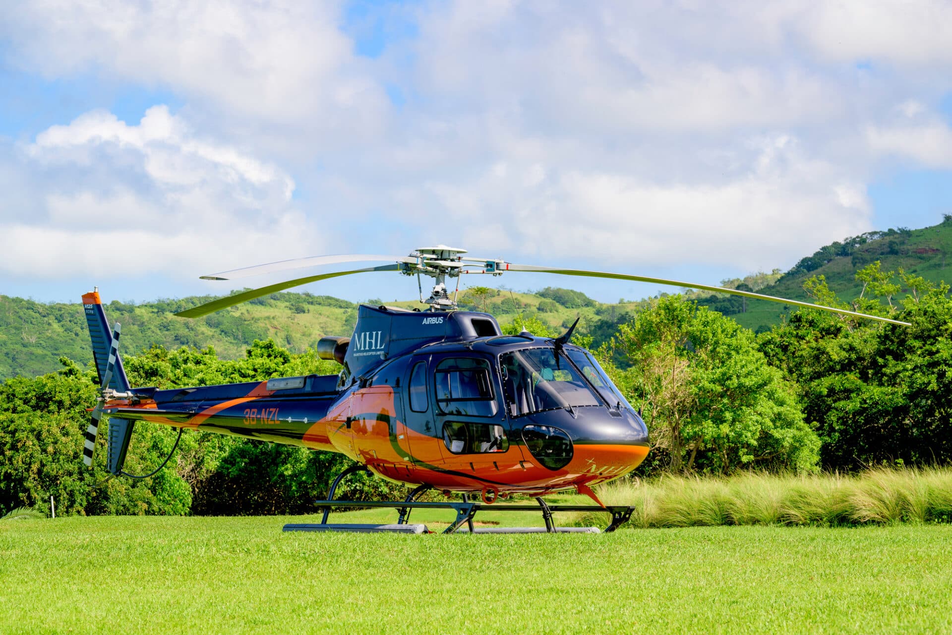 Blue and orange MHL helicopter on a helipad surrounded by green hills